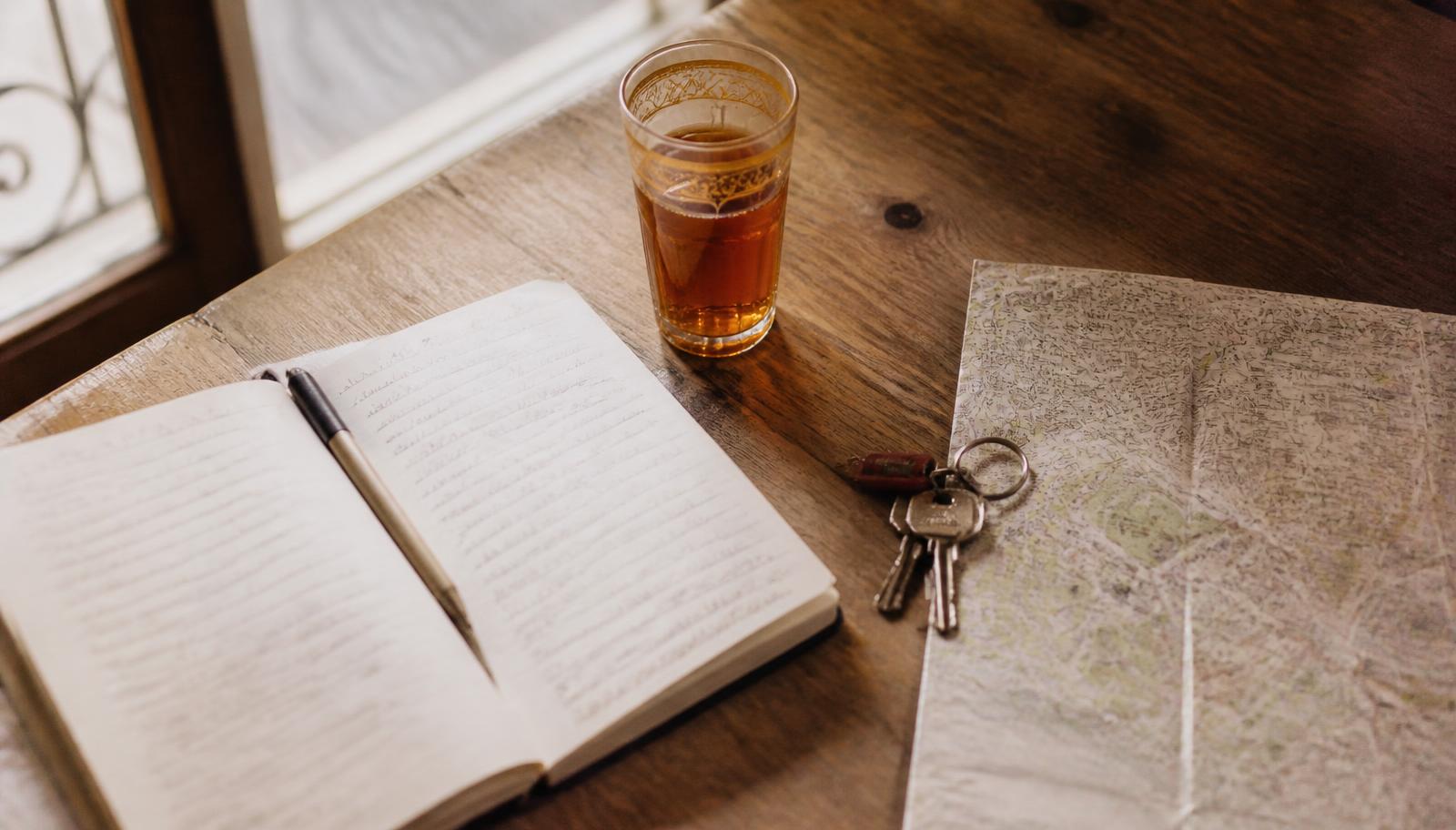 Notitieboek, muntthee, sleutels en een landkaart op een houten tafel